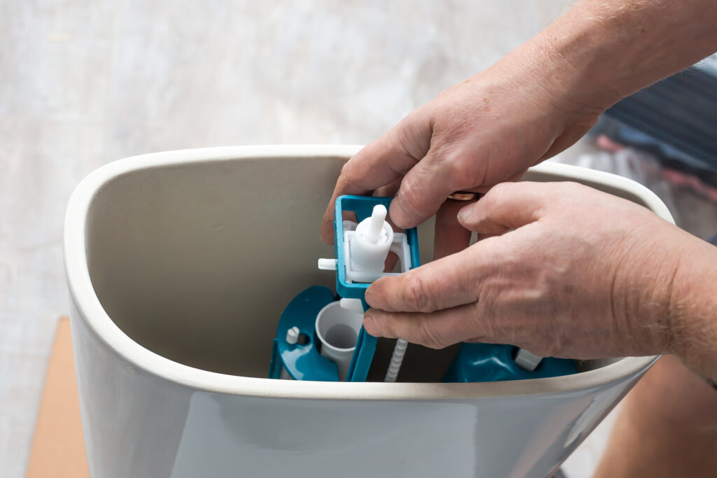 A plumber's hands shown replacing a pump in a toilet