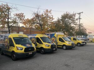 image3 1 - Brian B. Quick Line of yellow branded vans parked in a lot with autumn trees and power lines overhead in the background.