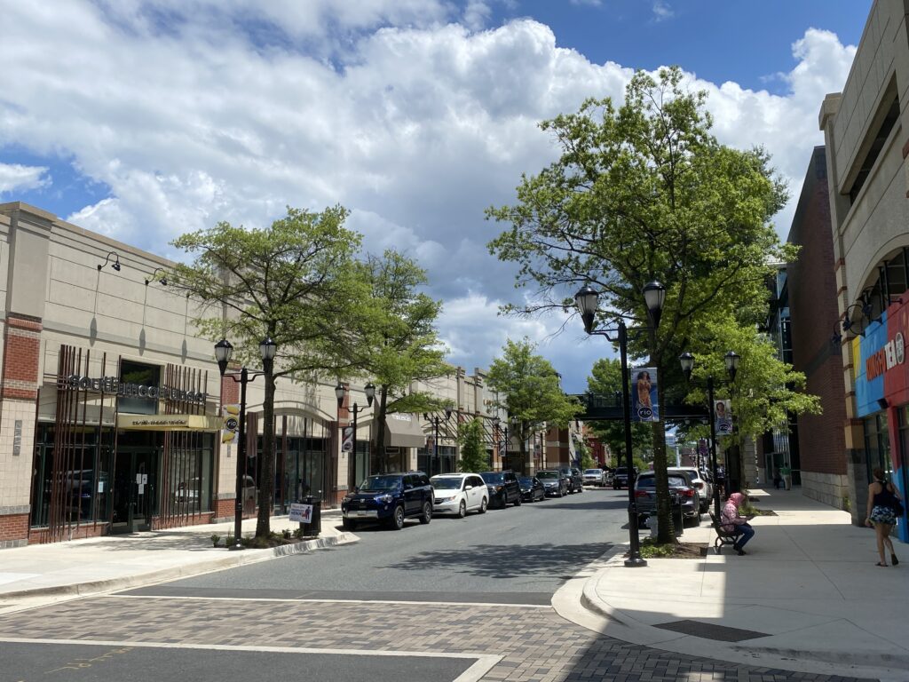 gaithersburg-maryland - Brian B. Quick Street scene in a shopping district with trees, parked cars, and beige storefronts under a partly cloudy sky.